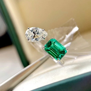 Detailed view of the emerald-cut green gemstone and pear-cut diamond on a silver ring band