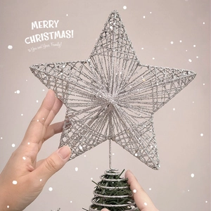 Hands placing a silver glittered metal star topper on top of a Christmas tree with bokeh