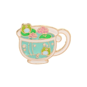 Detail of frog enamel pin featuring a white teacup with lotus flower and green frogs