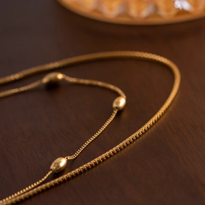 Close-up of double-layer gold box chain and oval bead necklace on a dark wood background
