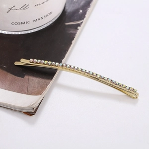 Golden bobby pin with iridescent AB rhinestones shown in a side view on a desk