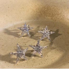 Detailed view of four silver starfish earrings with cubic zirconia on beige ceramic background