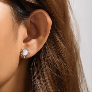 Macro shot of silver sunflower stud earrings with opal stone center on model's ear