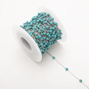 Détail de perles turquoise avec chaîne plaquée or 18K enroulée sur une bobine blanche