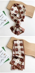 Detail showing checkered coffee silk skinny scarf with heart patterns on a wooden stand