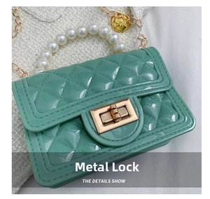 Detail of green jelly bag featuring pearl handle, gold hardware lock and chain