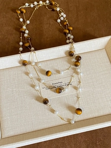 Detail of layered necklace featuring tiger eye stones, pearls, and gold metal chains
