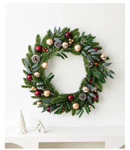 Detailed Christmas wreath featuring red and gold ornaments on a snowy pine needle base