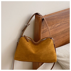 Close-up of caramel suede shoulder bag with silver hardware on a wooden headboard