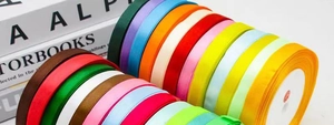 Close-up of 1cm colorful satin ribbon rolls stacked with vibrant textures for gift wrapping