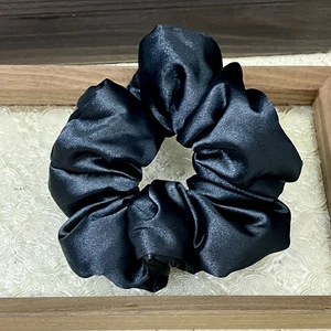 Close-up of black satin scrunchie with smooth silk texture and elegant vintage folds