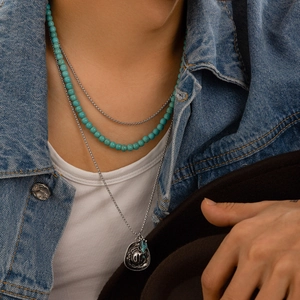 Detail of turquoise bead necklace and silver cowboy hat pendant on denim jacket