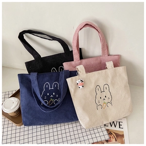 Flat lay of four colorful corduroy tote bags with cute bunny embroidery on checkered cloth