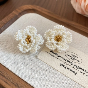 Close-up of handmade camellia earrings with intricate white beadwork and gold accents