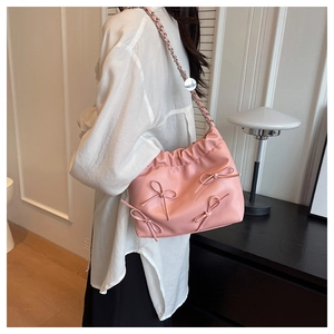 Pink bucket bag with bow detailing and silver chain strap shown as a crossbody bag