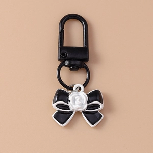 Detailed view of metal keychain with a stylish black bow and white resin rose pendant