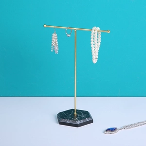 Minimalist gold T-bar jewelry display stand with a black marble base and various jewelry