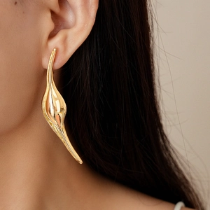 Detailed close-up of a high-polished golden flowing leaf earring worn by a female model