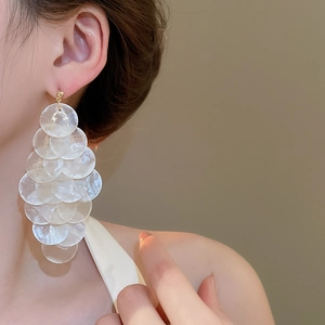 Macro detail of layered shell fringe earrings in gold finish worn by a model