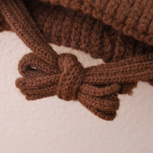 Macro shot of brown chunky knit hat showing delicate bow detail and wool texture