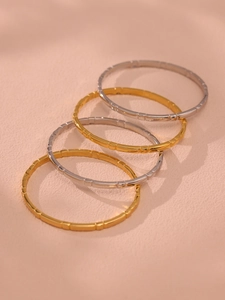 Close-up of four stacked gold and silver bangles with geometric textured patterns