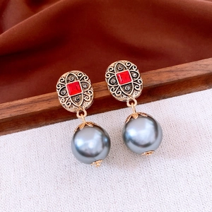 Detail of vintage gold earrings with red gemstones and large grey pearls on white fabric