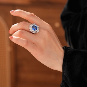 Dettaglio anello vintage con gemma blu ovale e corona di diamanti sulla mano