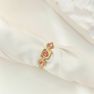 Detail view of a gold geometric ring with pink zircon stones on white silk fabric