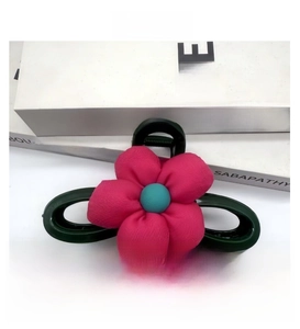 Détail d'une pince à cheveux fleur rose en tissu avec base vert foncé sur livre