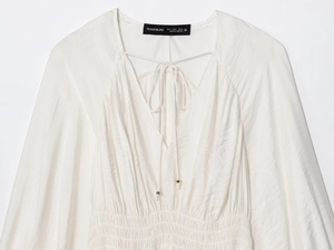 Detailed macro shot of the V-neck crossover lace-up and pleated texture of this white shirt
