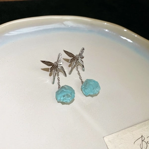 Detailed view of silver butterfly studs with light blue resin stone pendants on ceramic