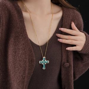 Close-up of golden cross pendant necklace with green gemstone and zircons on a model