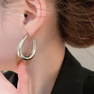 Close-up of a silver U-shaped chunky earring with a high-polish finish on a model