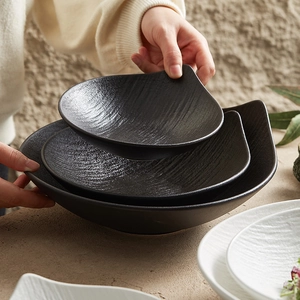 Three leaf-shaped black ceramic salad bowls with textured surface held by hands