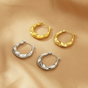 Polished gold and silver twisted hoop earrings on shimmering textured fabric backdrop