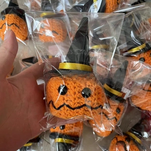 Close-up of handmade crochet Halloween pumpkin with a black witch hat in plastic packaging
