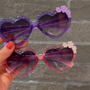 Close-up of heart-shaped kids sunglasses with purple glitter and flower decorations