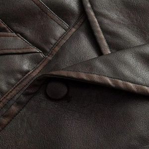 Detail of dark brown leather jacket featuring textured stitching and a leather-covered button