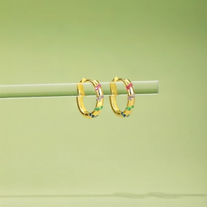Detailed close-up of gold hoop earrings featuring multi-color rainbow gemstones on green