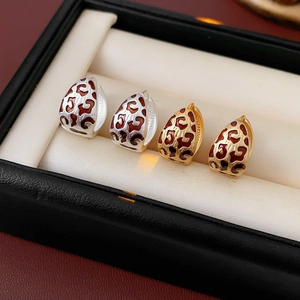 Detailed view of teardrop earrings with red leopard print enamel in gold and silver finish