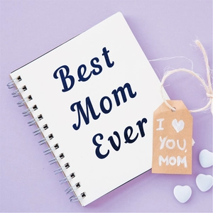 Detail of white spiral notebook with Best Mom Ever text and kraft gift tag on lilac surface