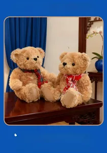 Close-up of two light brown teddy bears wearing red plaid scarves on a wooden table