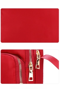 Detail showing red nylon fabric texture and golden double zipper hardware of the bag