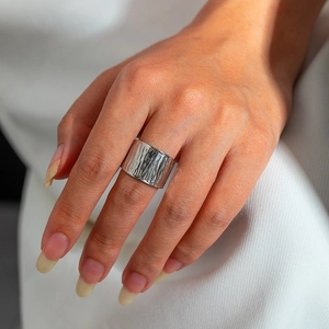 Close-up of a wide silver stainless steel ring with vertical texture on white fabric