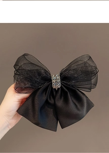 Detail of a large black mesh bow hair clip featuring a central silver rhinestone decoration