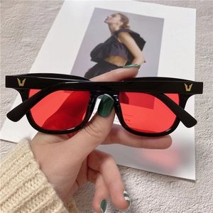 Close-up of black sunglasses frame with red lenses and metallic V-shaped logo detail