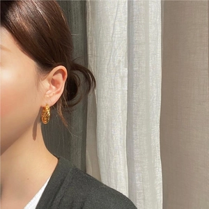 Detail of twisted gold hoop earrings worn by model in soft natural indoor lighting