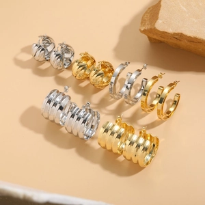Polished gold and silver C-shaped twist hoop earrings set on minimalist stone background