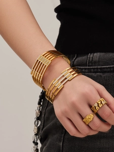 Dettaglio del bracciale rigido dorato a strati con zirconi e anelli a cuore abbinati su modella