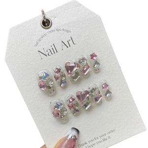 Sparkly handmade press-on nails with pink heart crystals and purple stars on a white card